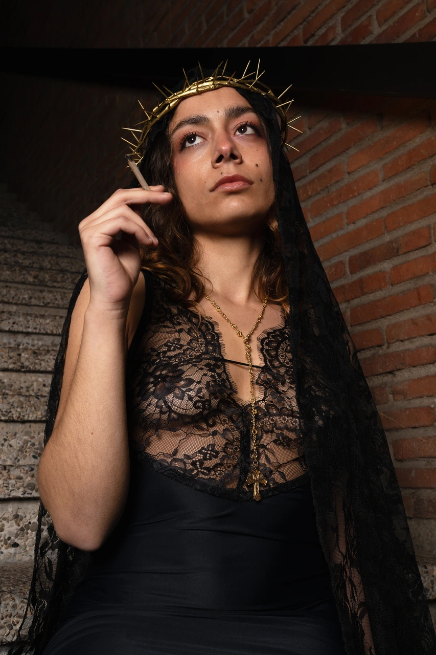 Retrat amb vel negre i corona de pues, davant d’una paret de maó.